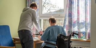 Eine Rollstuhlfahrerin und ein junger Mann in einem Patientenzimmer (Foto: IMAGO / Bihlmayerfotografie)