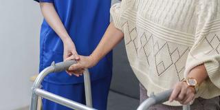 Eine Pflegekraft hält sanft die Hand einer älteren Person, die einen Rollator benutzt. (Foto: IMAGO / imagebroker    )
