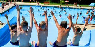 Badespaß im Schwimmbad. Bei Hitze springen Kinder von einer Rutsche in das blaue Wasser. (Foto: IMAGO / Eibner)
