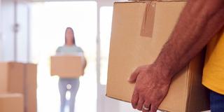 Zwei Personen tragen Umzugskisten in eine Wohnung. (Foto: IMAGO / Shotshop)