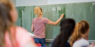Eine junge Grundschullehrerin schreibt etwas an die Tafel (Foto: dpa)