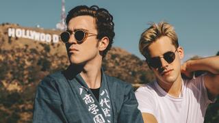 Zwei junge Männer stehen vor Bergen und werden von der Sonne angestrahlt, im Hintergrund lässt sich das "Hollywood"-Sign erkennen. (Foto: Pressefoto/Ofenbach)