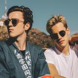 Zwei junge Männer stehen vor Bergen und werden von der Sonne angestrahlt, im Hintergrund lässt sich das "Hollywood"-Sign erkennen. (Foto: Pressefoto/Ofenbach)