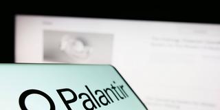 Ein Handy auf dem Palantir zu lesen ist - im Hintergrund ein Computerbildschirm. (Foto: IMAGO / Zoonar)