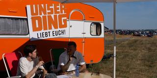 Kontra K im Interview vor dem orangenen UNSERDING-Wohnwagen. (Foto: UNSERDING/Katharina Weber)