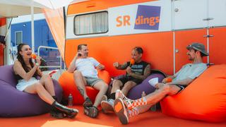 Vier Menschen sitzen auf Sitzsäcken vor einem orangenen SRdings-Wohnwagen (Foto: MxM Photo)