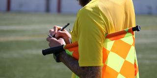 Ein Schiedsrichter mit Fahne unter dem Arm schreibt auf seine Schiedsrichterkarte (Foto: pixabay.com/taniadimas)
