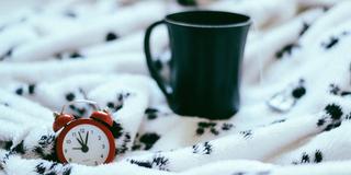 Ein Wecker und eine Tasse auf einer Bettdecke (Foto: pixabay.com/stocksnap)