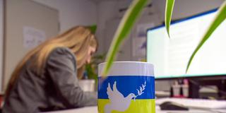 Eine Kaffeetasser mit der ukrainischen Flagge und einer Friedenstaube steht auf einem Bürotisch (Foto: SR)