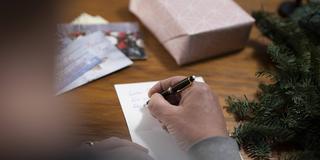 Ein Mann schreibt eine Weihnachtskarte (Symbolbild) (Foto: IMAGO / photothek)