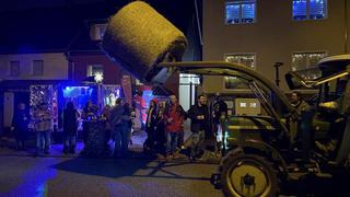 Ein Traktor mit einem Heuballen steht vor einem Platz mit Leuten. (Foto: UNSERDING)