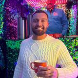 Ein Mann mit einem weißen Pulli hält eine orangene Tasse in der Hand (Foto: UNSERDING)