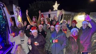 Eine Gruppe von Menschen steht mit Weihnachtsmannmützen neben dem Weihnachtsmobil und wirft fröhlich die Hände in die Luft. (Foto: UNSERDING)